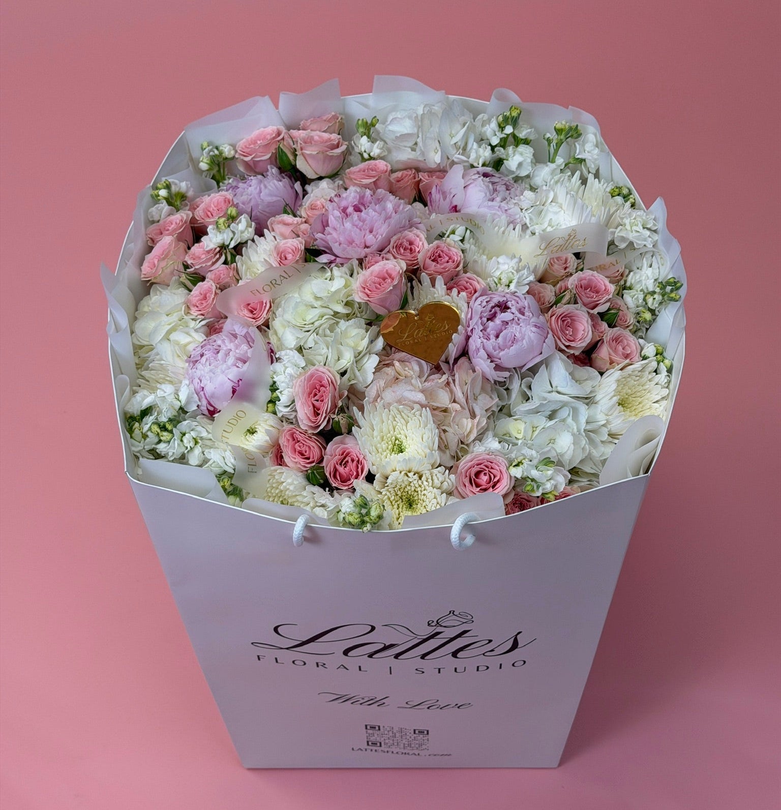 A large floral bouquet in a white gift box with the brand name 'Lalies Floral Studio' printed on the front, set against a solid pink background.