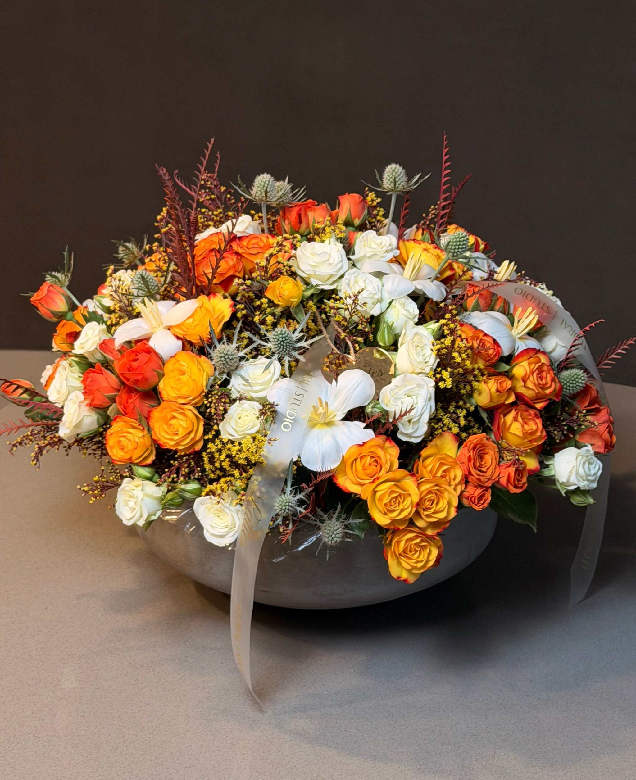 Autumn Glow Arrangement with orange roses, white roses, white tulips, golden accents, thistles, and greenery centerpiece