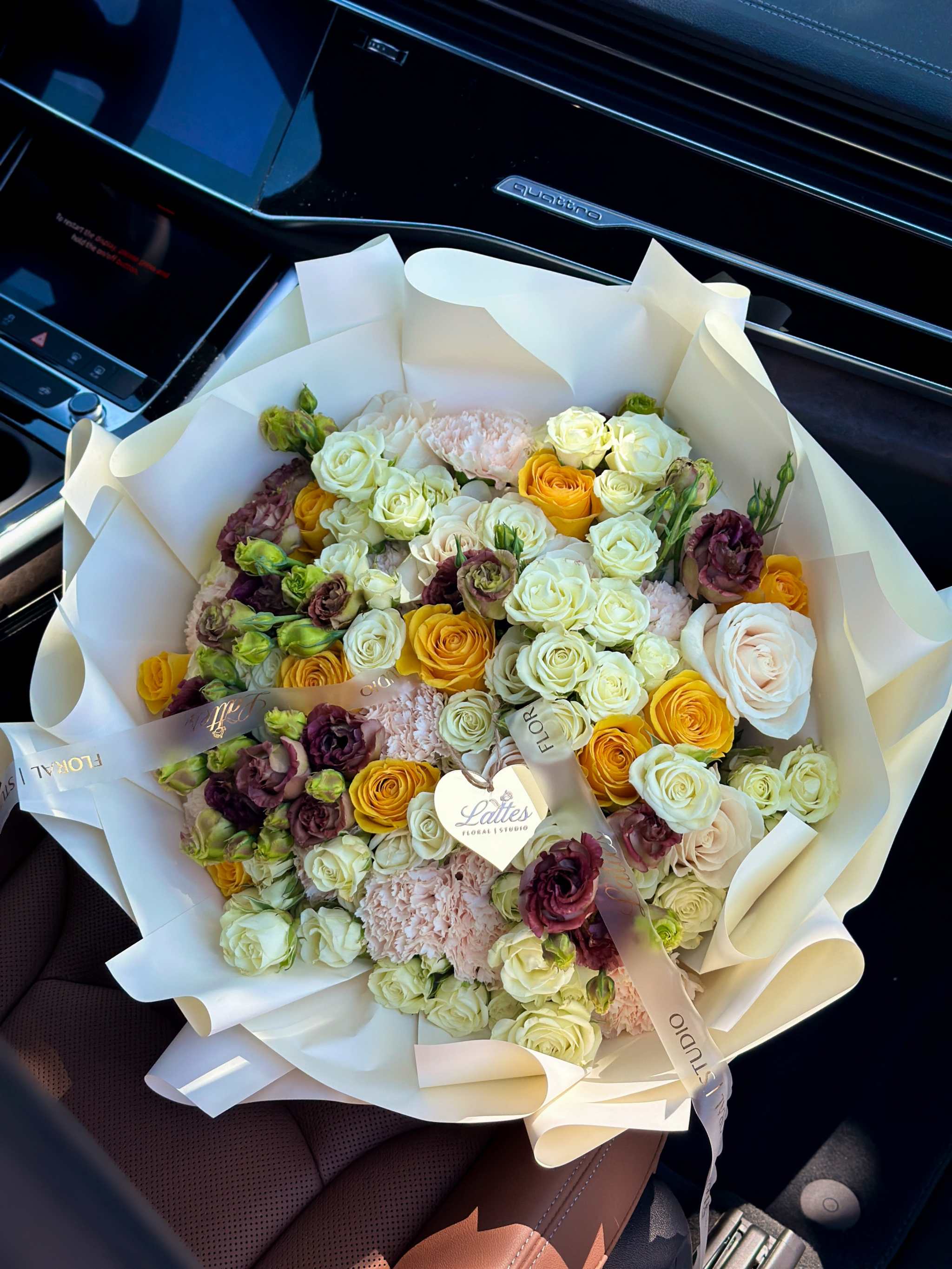 Golden Crème bouquet with yellow and white roses, lisianthus, and brown-chocolate blooms in creamy white wrapping
