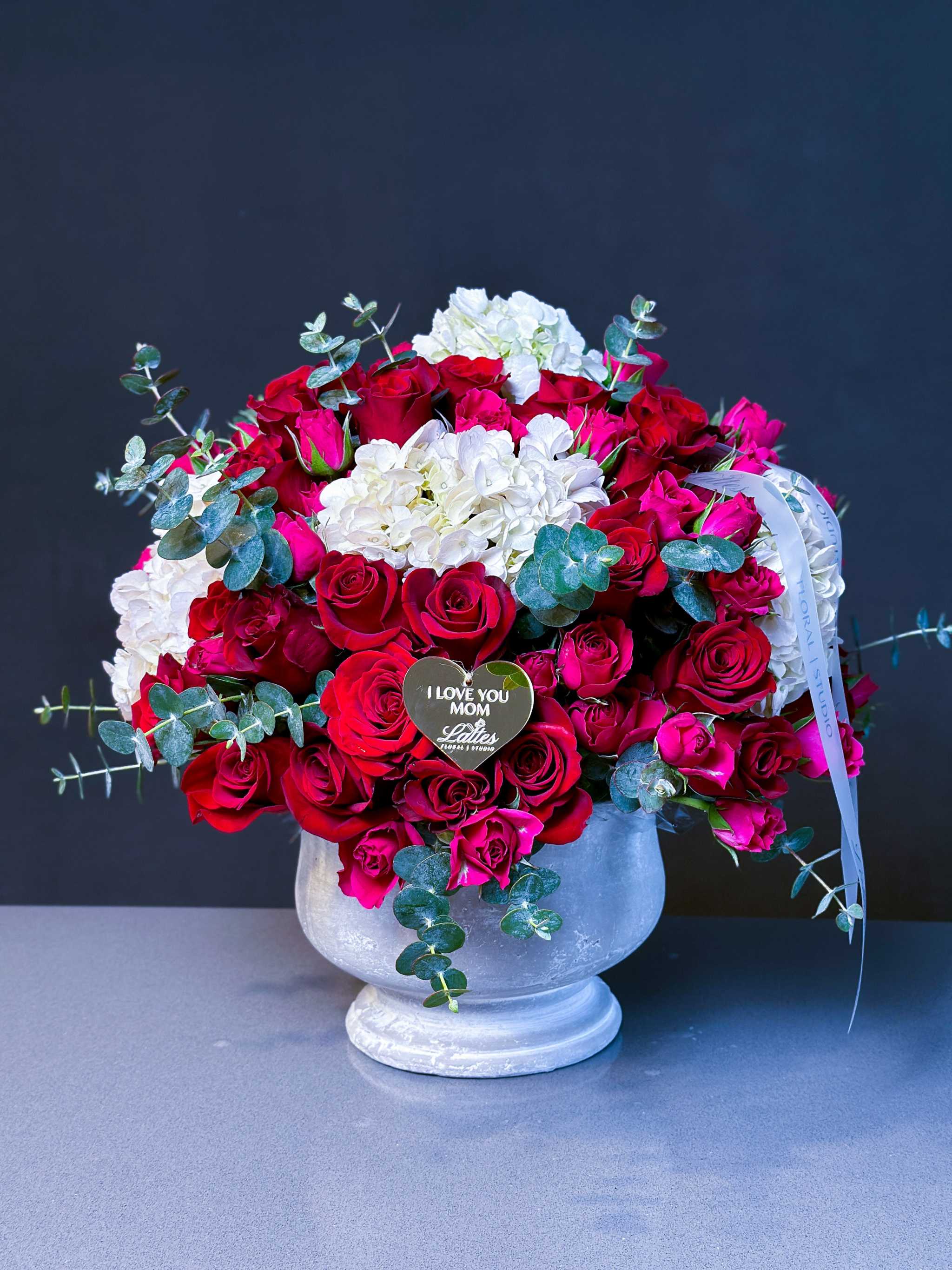 Luxurious floral arrangement with deep crimson roses, spray roses, and white hydrangeas in an elegant vase