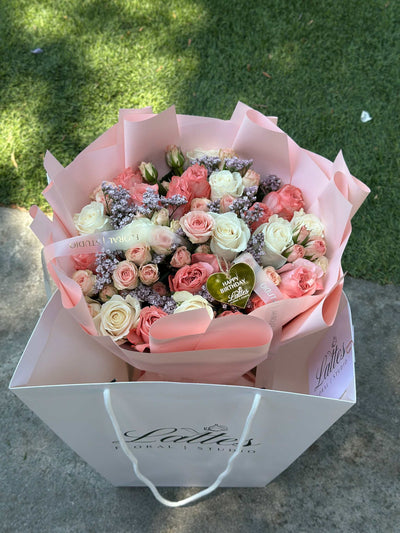 Romantic bouquet with pink roses, white roses, and spray roses in blush pink wrapping