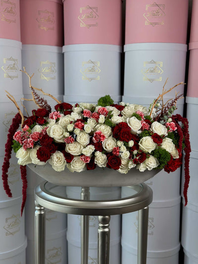 Imperial Romance floral arrangement with red and white roses, pink carnations, hanging amaranthus, and sculptural branches in an elegant elongated vase