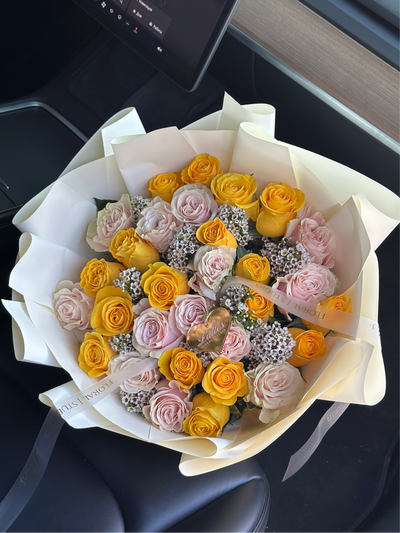Sunlit Bloom bouquet with yellow and blush roses and wax flowers wrapped in ivory paper
