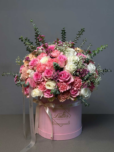 A luxurious floral arrangement featuring roses in shades of pink and white, carnations, waxflowers, and eucalyptus sprigs in a pink box 