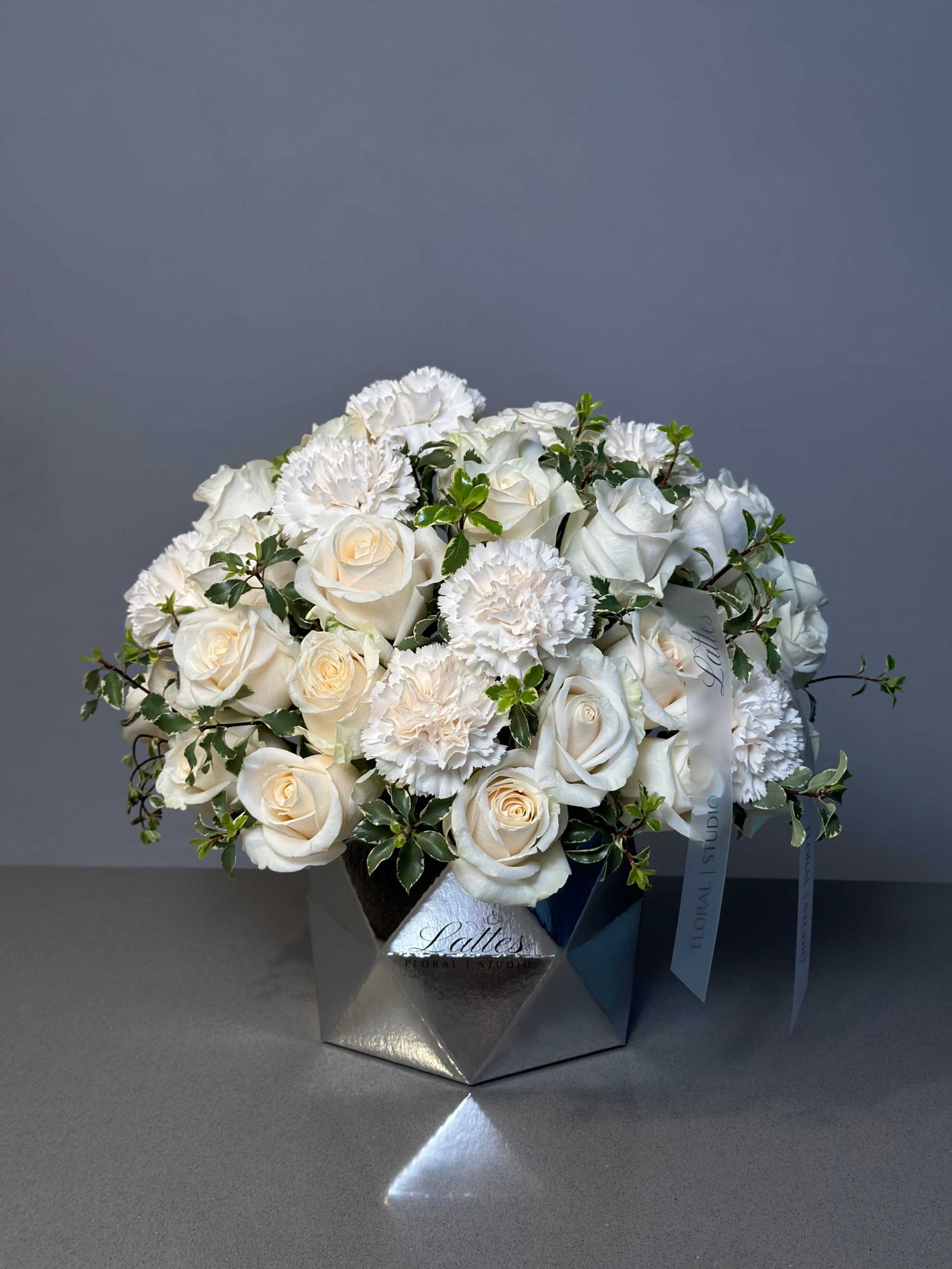 White Floral Poetry arrangement with white roses, carnations, fresh greenery in silver geometric vase