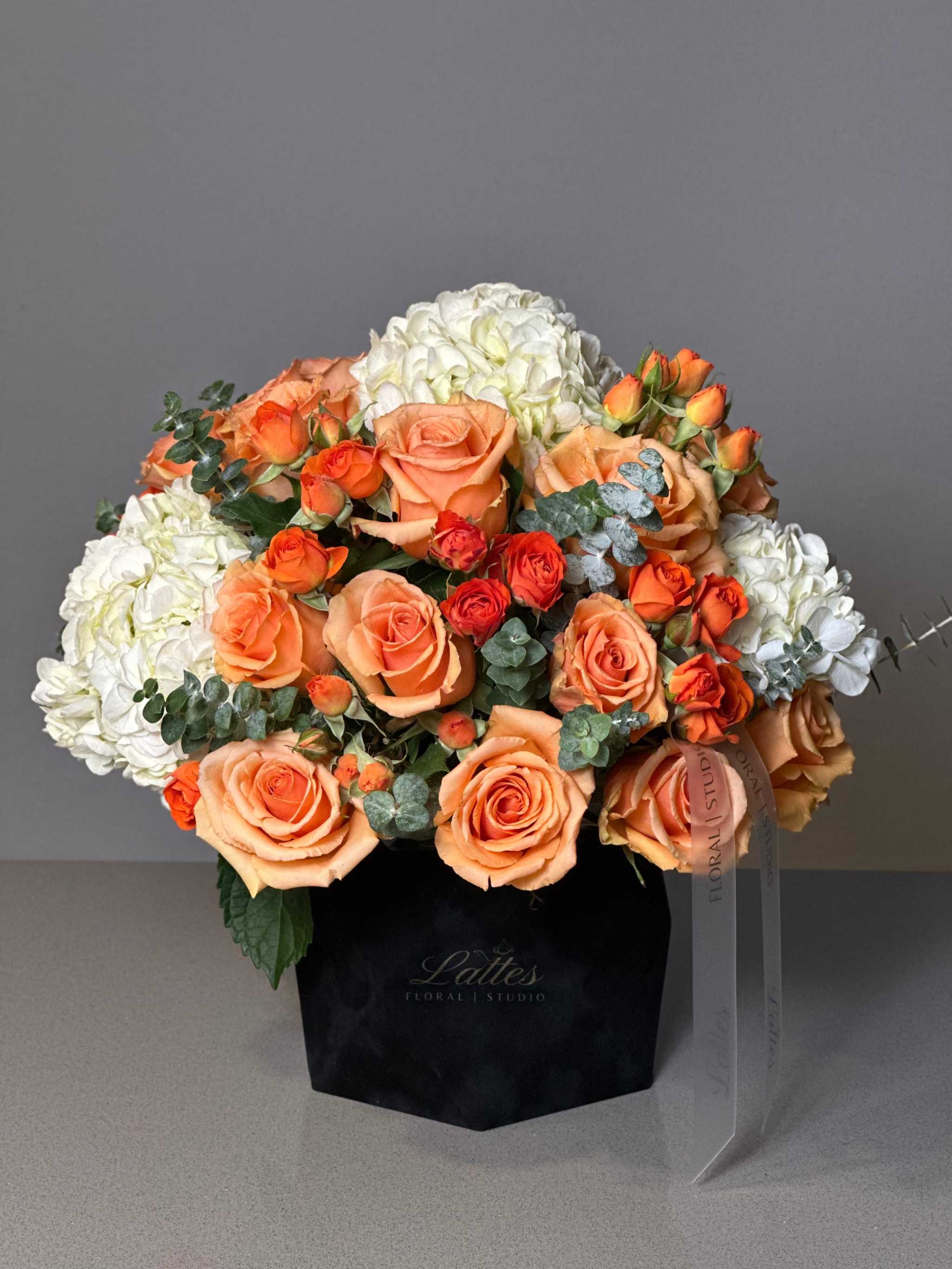 Whispers of Spring Flower Box with orange roses, white hydrangeas, and eucalyptus in a sleek black box.