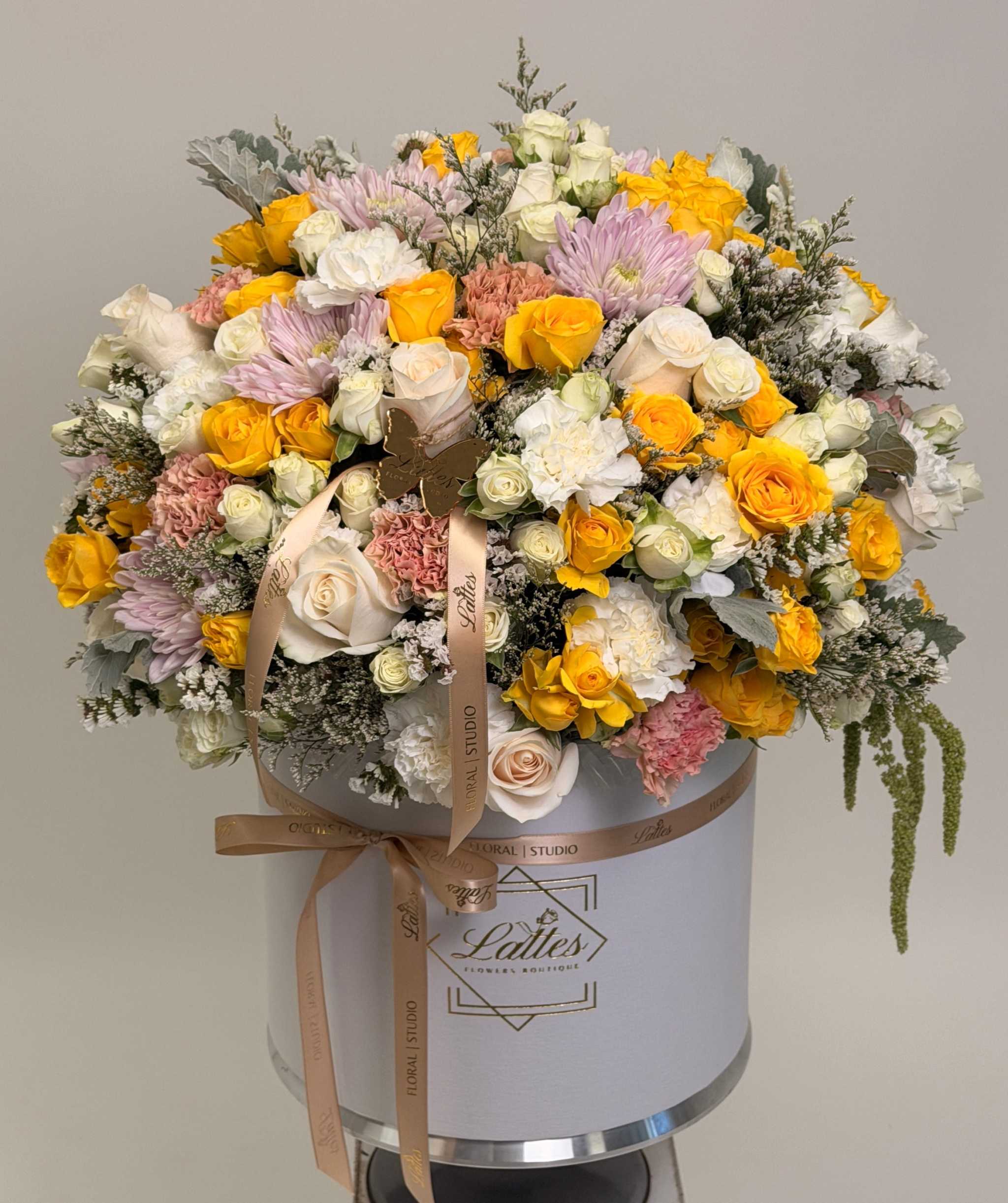 Amore floral arrangement with yellow and blush roses, pink chrysanthemums, and carnations in an elegant hatbox
